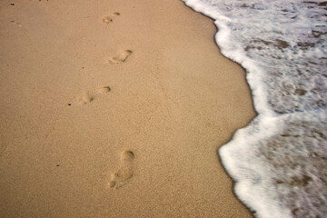 Footprints in Sand with Ocean Wave – Tranquil Beach Scene Symbolizing Journey and Passage of Time.