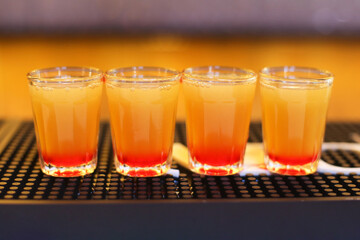 Colorful party shots. Vibrant drink glasses. Red and orange cocktail. Sweet alcoholic drinks. Fun celebration concept. Bar counter scene. Festive atmosphere. Bright beverage presentation.