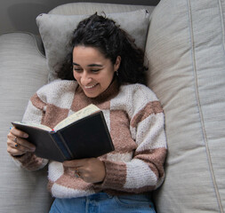 Brunette girl sitting on sofa while reading and laughing