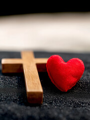 A wooden cross lies next to a red heart, representing the union of love and faith