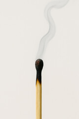 A partially burnt matchstick with the top glowing red and a thin trail of smoke curling upward, shot with a minimalistic white background