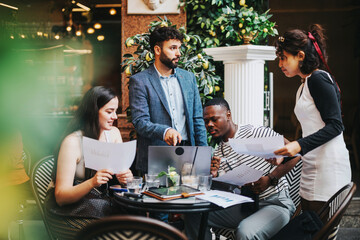 A diverse group of business professionals engages in a productive meeting, strategizing and discussing projects over coffee in a stylish modern cafe.
