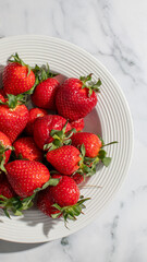 Fresh ripe strawberries in a white plate on marble, embodying summer harvest and healthy eating concepts