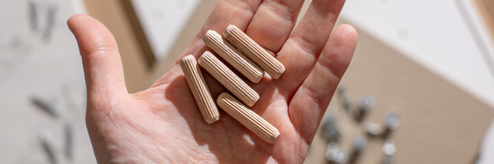 Hand holding wooden dowels, carpentry work essentials, DIY home projects, creative woodworking supplies, tool background craftsmanship
