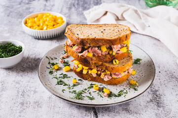 Tuna and corn salad on grain bread on a plate on a table