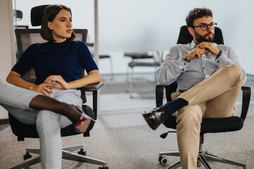 Obraz premium A man and a woman in business attire are seated in an office. They appear engaged in a serious discussion, reflecting a professional work environment. The office setting is modern and minimalistic.