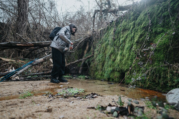 A hiker extensively equipped with a backpack and outdoor wear carefully filtering water from a...