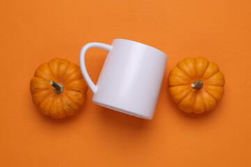White ceramic cup and pumpkins on orange background