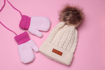 Children's knitted mittens on strings and a hat with a balabon, pink background