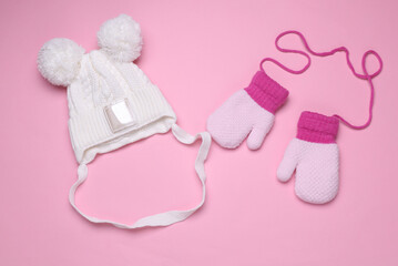 Children's knitted mittens on strings and a hat with a balabon, pink background
