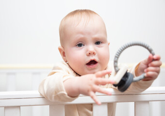 Cute baby playing with rattle in crib