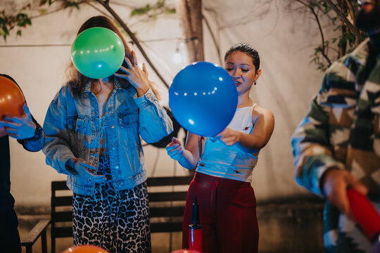 A group of young friends inflating colorful balloons during a lively party outdoors.