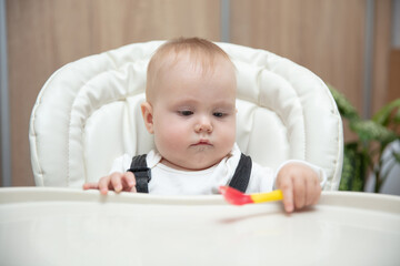 Portrait of cute baby with spoon sitting at feeding table