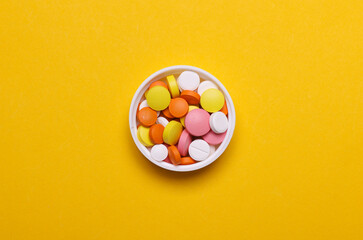 Obraz premium Many colorful tablets in a cap on a yellow background. Top view
