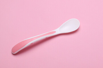 Plastic spoon for feeding baby on pink background