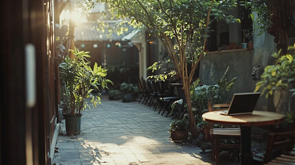 A tranquil outdoor cafe scene with a laptop, plants, and inviting natural sunlight.
