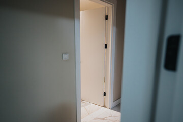 A close-up view of a partially opened modern white interior door in a residential space, with light softly illuminating the tiled flooring inside.