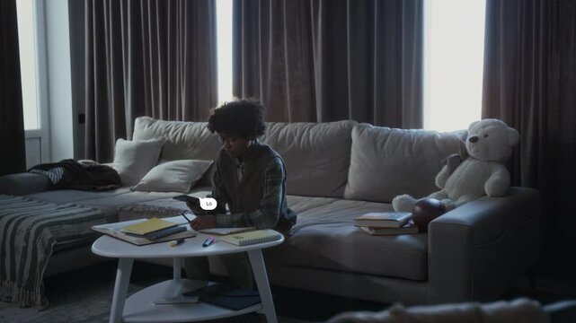 Full shot with VFX video effects of teenage African American boy sitting at home, trying to concentrate on homework, distracted by hateful messages popping up, crying in despair