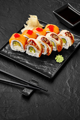 Sushi set presenting salmon philadelphia and eel uramaki rolls with soy sauce on black background