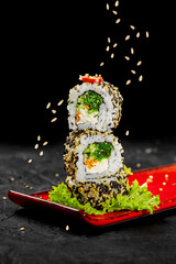 Stack of uramaki sushi rolls with sesame seeds falling on a red plate © nazarovsergey