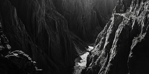 A dramatic landscape featuring a narrow, dark canyon with steep walls and a vanishing point into the distance. The image is in black and white, adding to the sense of depth and mystery. This photo
