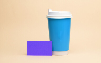 Blue disposable coffee cup and purple business card on a yellow background. Template for branding