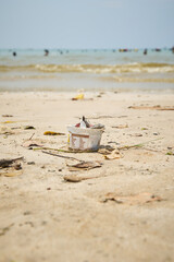 discarded plastic cup lying on beach sand, used for ice cream or yogurt left behind by visitors, pollution, human impact on nature, environmental awareness theme, soft focus with copy space