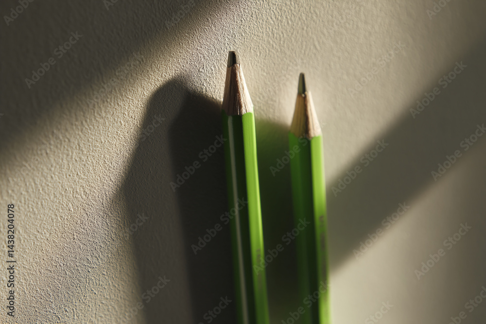 Poster close-up of two green pencils, sharpened tips visible, against a textured beige background, illumina