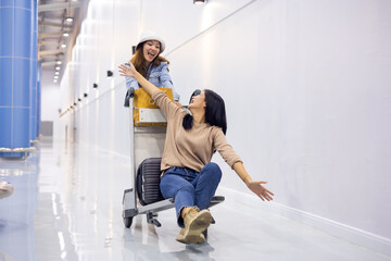 Riding baggage trolley. two Happy Asian beautiful woman passenger traveler and friends having fun...