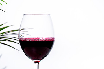 Non-alcoholic, alcohol free, red wine cabernet sauvignon in glass White background, palm leaves shadows, hard light