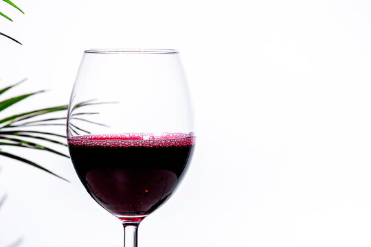 Non-alcoholic, alcohol free, red wine cabernet sauvignon in glass White background, palm leaves shadows, hard light