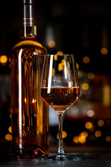 French pink rose wine syrah in glass and wine bottle on dark bar background with bokh lights