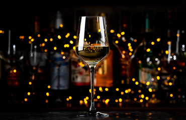 White Chardonnay wine glass and wine bottles on dark bar background with lights