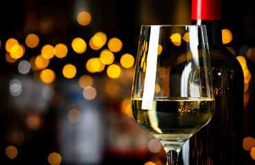 German dry white riesling wine in  glass and wine bottle on dark bar background with lights