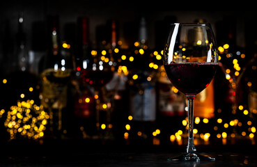 Italian dry red wine sangiovese in glass and wine bottles on dark bar background with lights