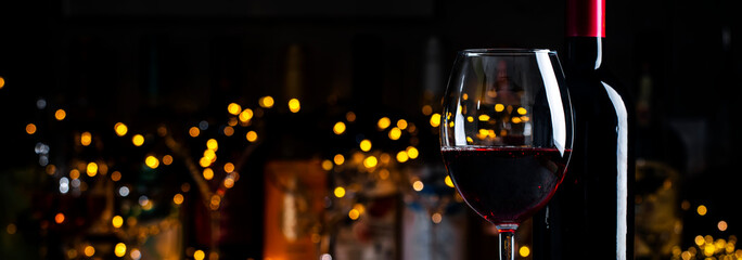 Dry red wine Cabernet Sauvignon in glass and wine bottle on dark bar background with lights