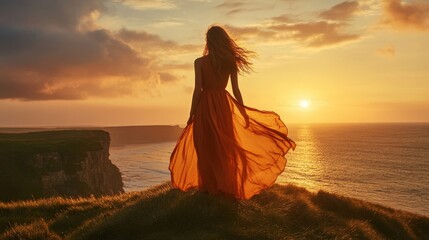 Woman in flowing orange dress at sunset over ocean cliffs