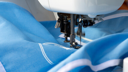 Guiding light blue fabric under the needle of a white embroidery machine. The machine is actively...