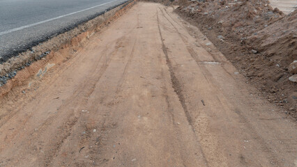 Dirt road or construction site next to a paved road. Dirt area has tire tracks and loose soil...