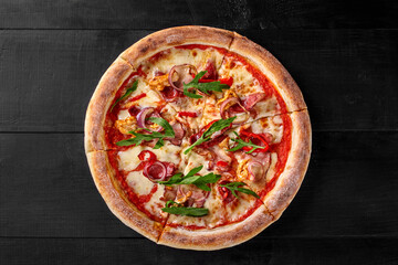 Delicious pizza with chicken, bacon, arugula and mozzarella on black wooden table