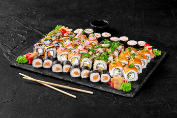 Sushi set with soy sauce, pickled ginger, wasabi and chopsticks on black stone plate
