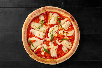 Delicious pepperoni pizza with melted mozzarella and chili pepper on black wooden table
