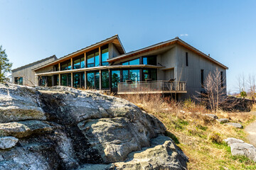 Kerhonkson, NY - US - Apr 23, 2025 Modern, wood-clad Minnewaska State Park welcome center with large glass windows sits beside stone outcrops, blending into the natural landscape under a clear sky.