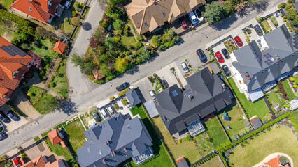 Aerial view of suburban houses in a green environment near a large metropolis, featuring modern single-family homes equipped with solar panels on their roofs.