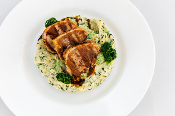 Savory dish featuring grilled meat with creamy spinach puree and fresh greens served on white plate