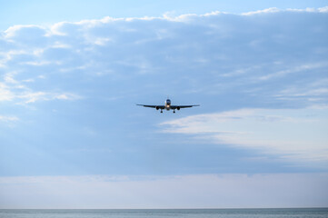 Passenger civil aircraft approaching landing over sea with landing gear and flaps extended against cloudy sky. Travel concept, landing difficult conditions, concept of landing in difficult conditions