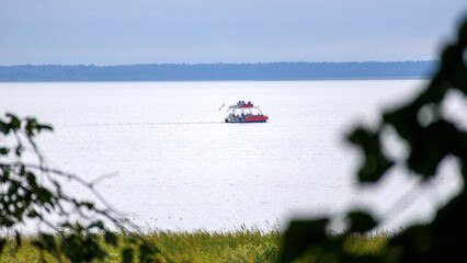 
A small, red boat with a white hull floats on a calm body of water in the distance, while blurred...
