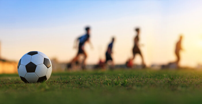 Fototapeta Action sport outdoors of kids having fun playing soccer football for exercise in community rural area under the twilight sunset sky.