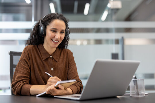 Successful businesswoman at online business meeting conference. Woman with headphones watching educational video course, writing data in notebook.