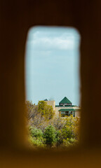 Through a wall opening, a traditional building in Fez appears, surrounded by trees under a bright,...